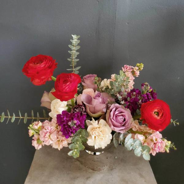 Mixed bouquet of roses, ranunculus, and pink blooms in a low vase