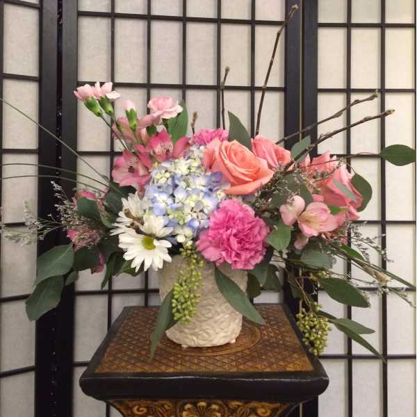 Pink and peach flowers arranged in a cream vase.