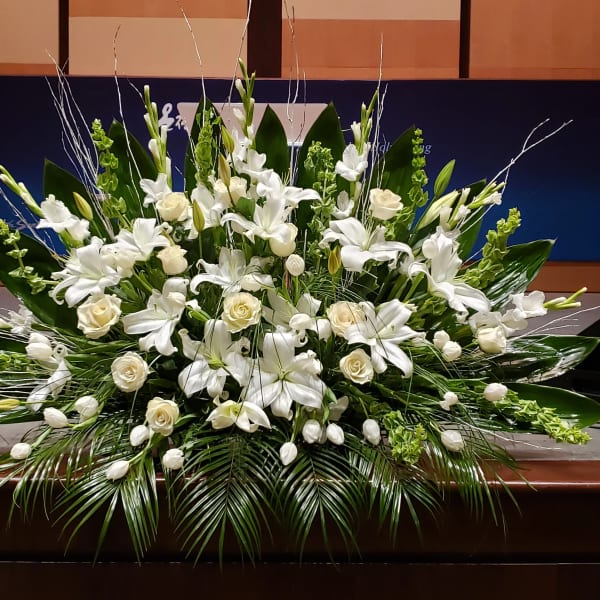 Large white lily and rose arrangement with tulips and Bells of Ireland in a low, fan-shaped design