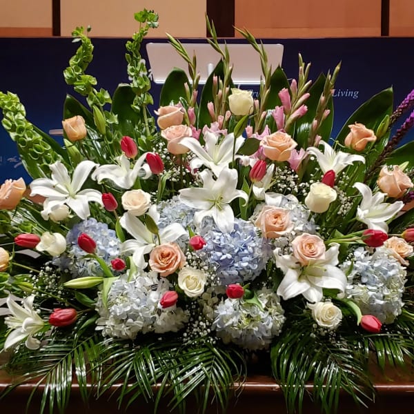 Large front-facing arrangement of white lilies, peach roses, blue hydrangeas, and pink tulips