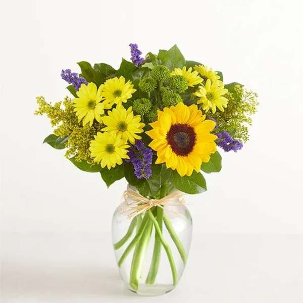 Yellow daisies and a sunflower in a clear glass vase