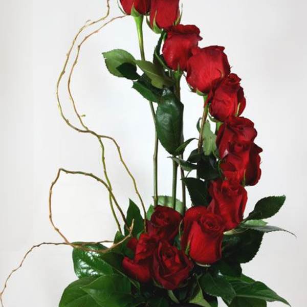 Tall arrangement of red roses in a black vase with curly branches