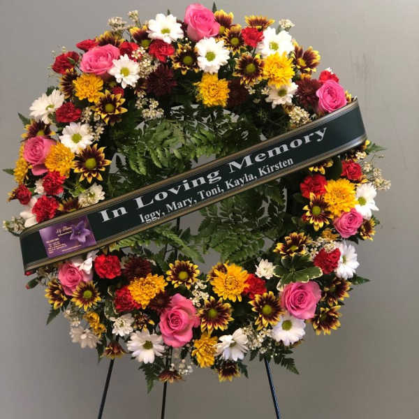 Circular sympathy wreath with pink roses, daisies, and mums on a stand
