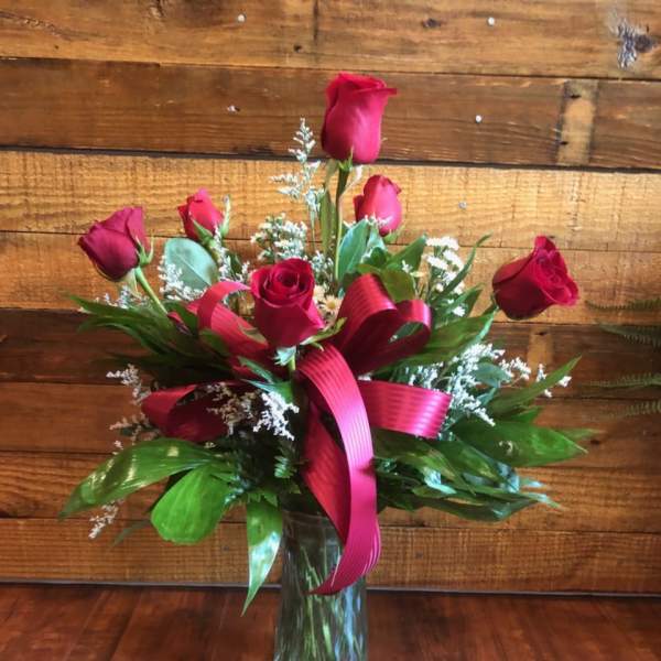 Red roses arranged in a clear glass vase with a pink ribbon