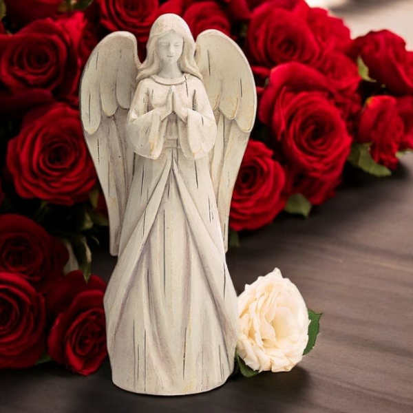 White angel figurine in front of red roses with a cream rose at the base