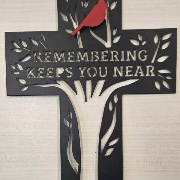 Black cross memorial sign with a red bird and the words "Remembering Keeps You Near"