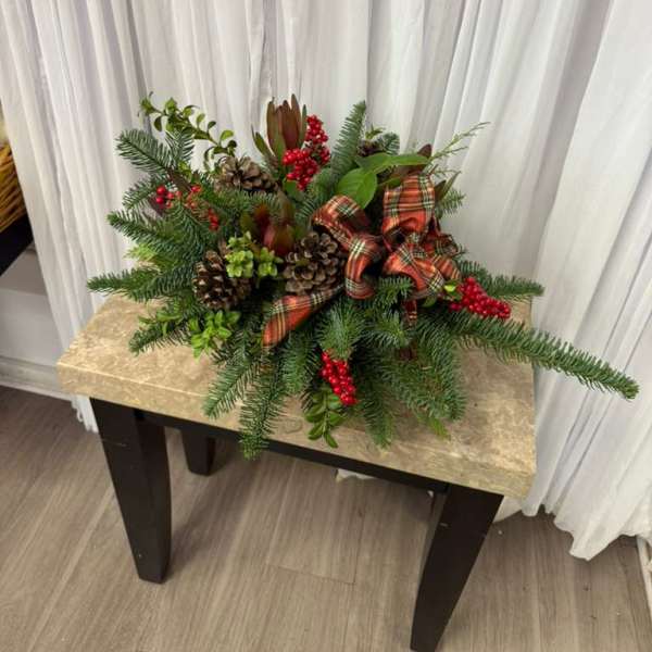 Holiday centerpiece with evergreen branches, pinecones, red berries, and a plaid bow