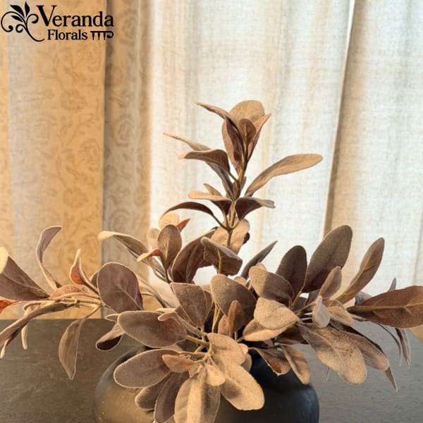 Muted brown faux foliage in a round black vase on a dark surface