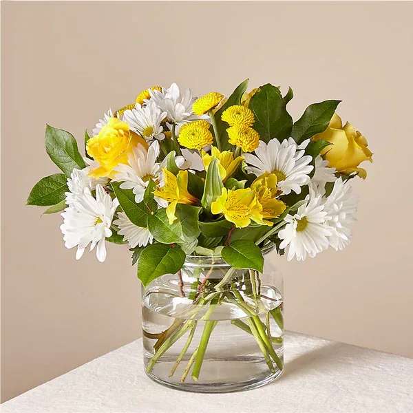Yellow and white flowers arranged in a clear glass vase