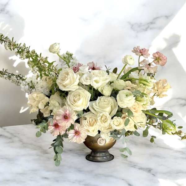 Cream and blush floral arrangement in a gold pedestal vase