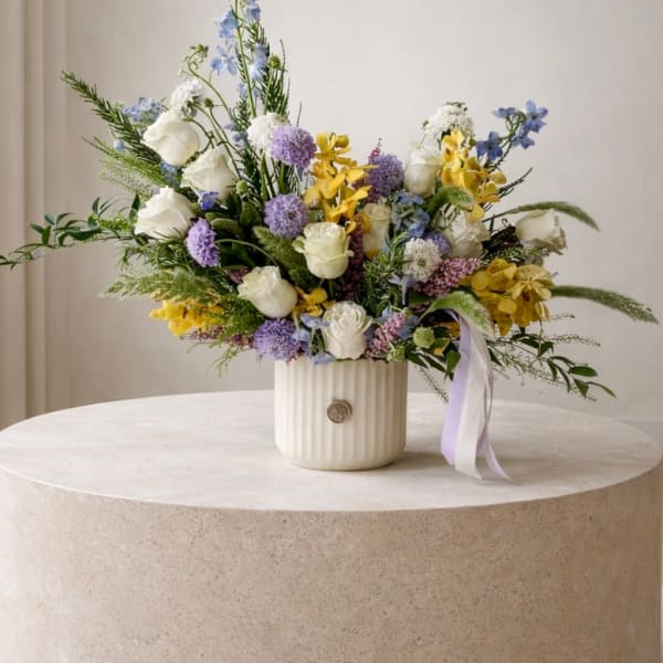 Mixed bouquet of white, yellow, and lavender flowers in a ribbed vase