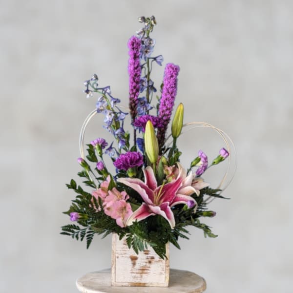Pink lily arrangement with purple and blue flowers in a rustic wooden box