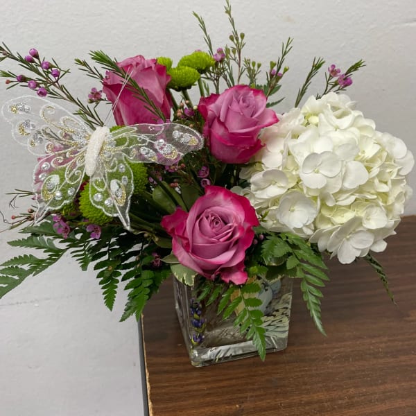 Pink roses and white hydrangea in a glass vase with a decorative butterfly