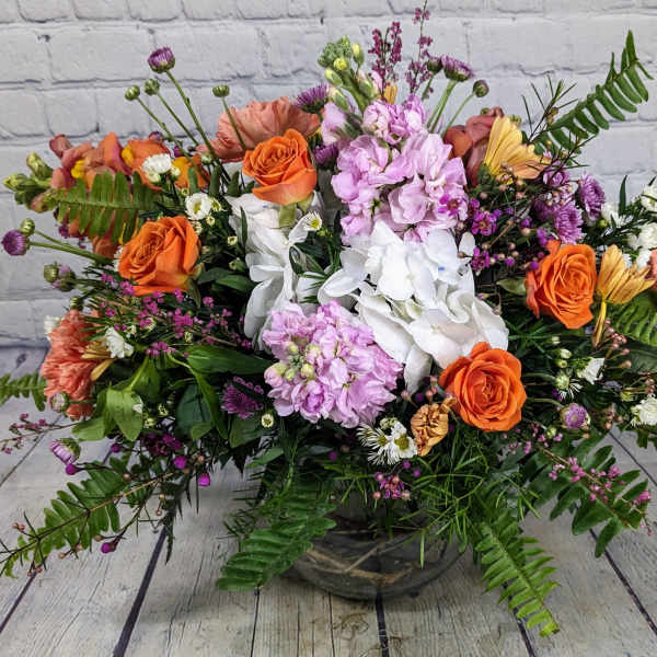 Mixed bouquet of orange and pink flowers in a low glass vase