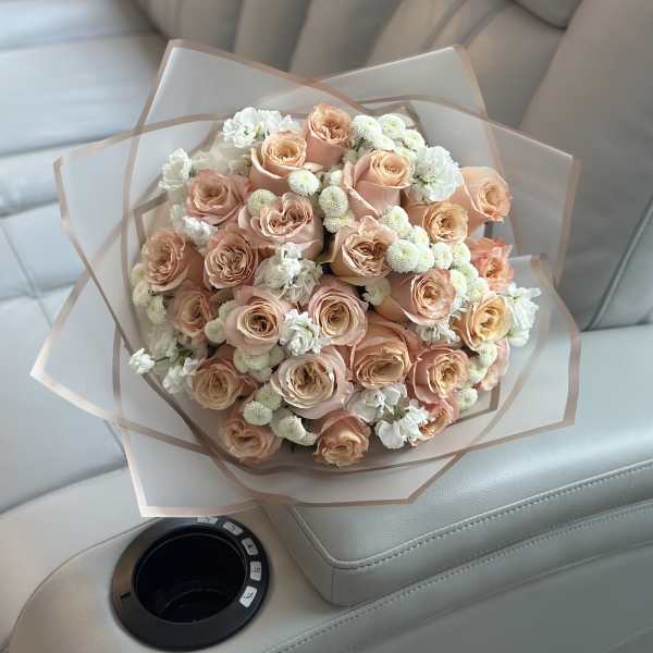 Bouquet of peach roses with white filler flowers wrapped in translucent paper