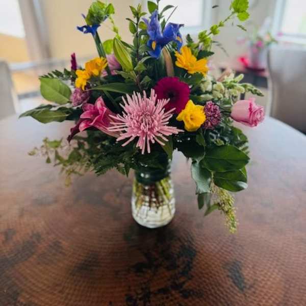 Mixed bouquet in a clear glass vase with pink, yellow, blue, and white flowers