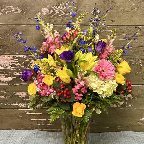 Mixed bouquet in a clear glass vase with yellow, pink, purple, and blue flowers