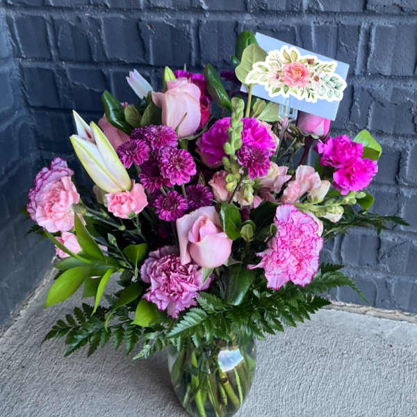 Pink and purple bouquet in a glass vase with a floral card