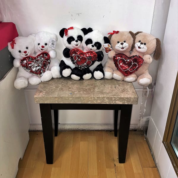 Three plush teddy bears and two panda plush toys holding red heart pillows on a table.