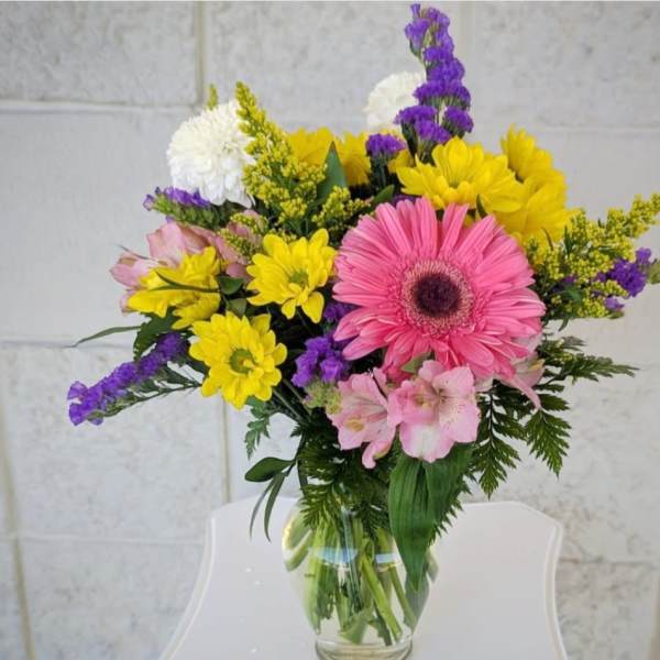 Mixed bouquet of pink, yellow, purple, and white flowers in a glass vase