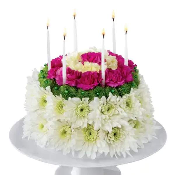 Round floral cake with candles and pink, white, and green flowers