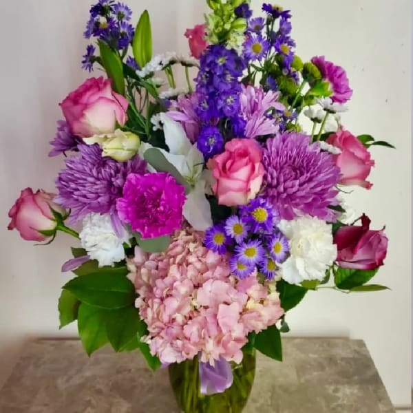 Mixed bouquet of pink roses, purple blooms, and hydrangea in a glass vase