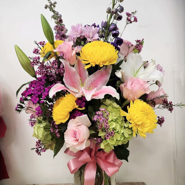 Mixed bouquet in a glass vase with pink roses, lilies, and yellow chrysanthemums
