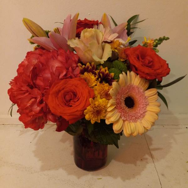 Mixed bouquet of red, pink, and yellow flowers in a dark glass vase