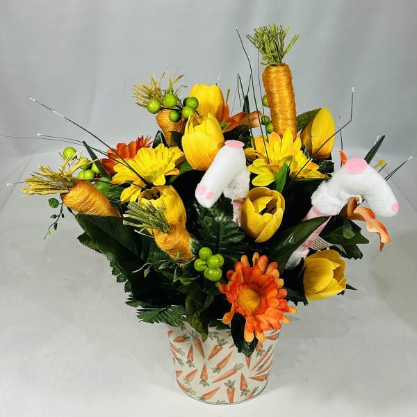 Yellow and orange floral arrangement in a carrot-patterned pot with plush bunny ears