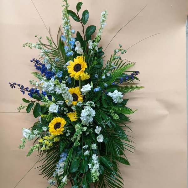 Standing floral spray with sunflowers, blue and white flowers, and greenery