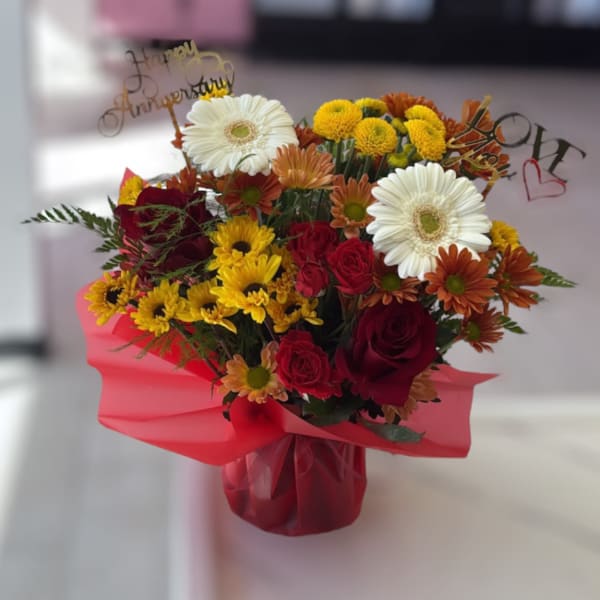 Bouquet of red roses, white gerbera daisies, and yellow mums in pink wrap