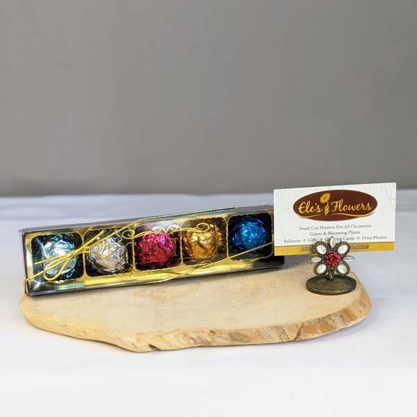 Rectangular box of foil-wrapped chocolates beside a business card on a wood display slab