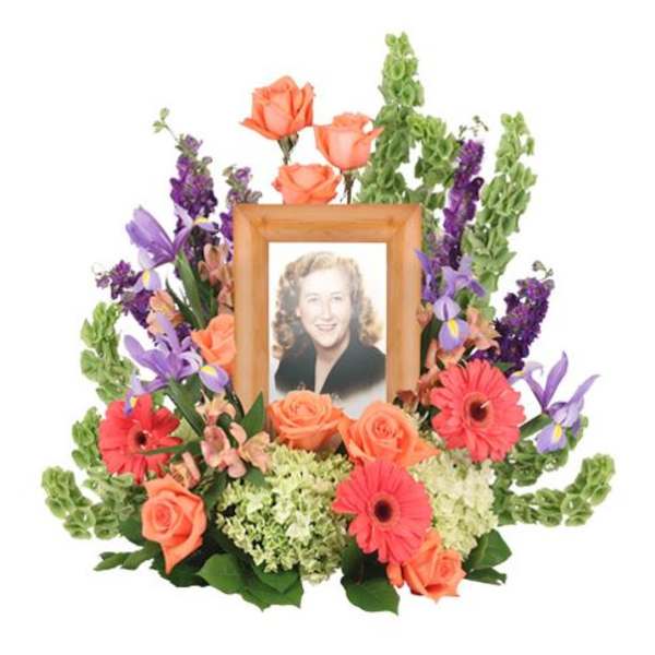 Framed portrait surrounded by orange roses, purple flowers, and pink gerberas