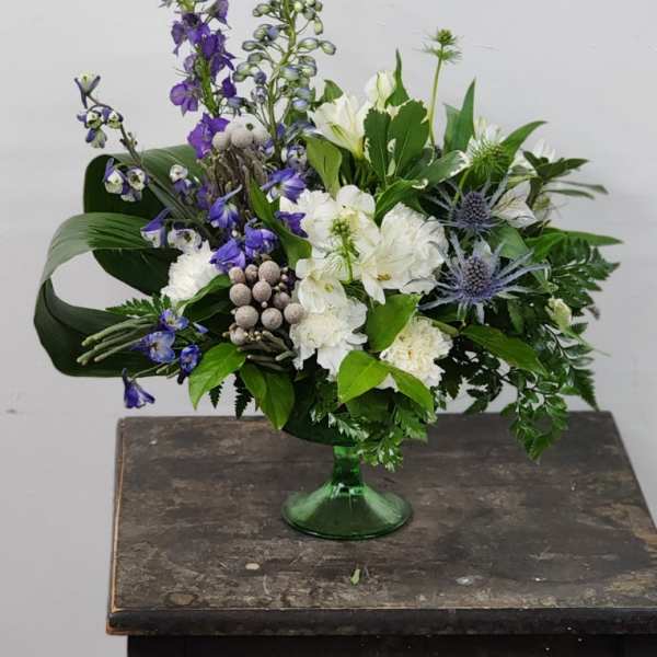 White and purple floral arrangement in a green glass vase