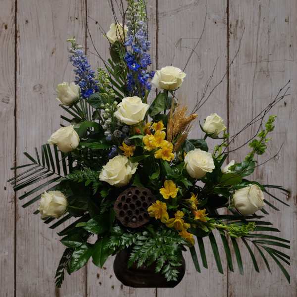 White roses with blue and yellow flowers in a black vase