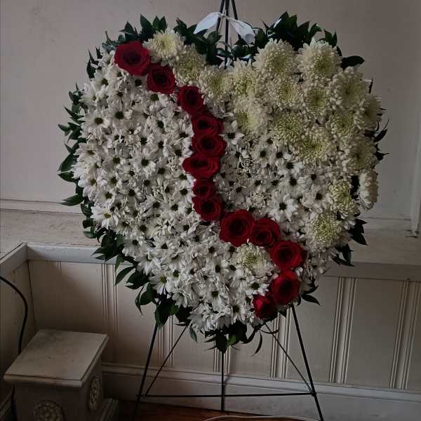Heart-shaped floral wreath with white daisies and red roses on a stand