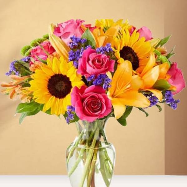 Bouquet of sunflowers, pink roses, and yellow lilies in a glass vase