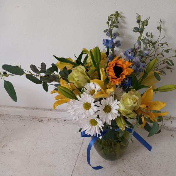 Mixed bouquet of yellow, white, blue, and orange flowers in a glass vase