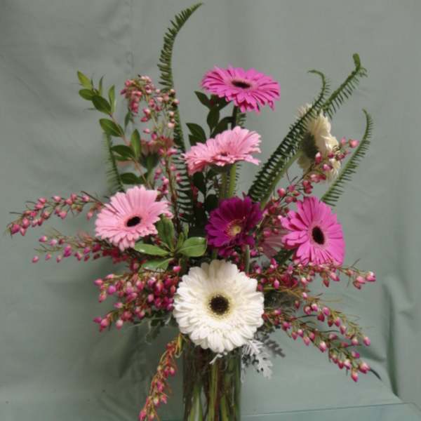 Tall glass vase of pink and white gerbera daisies with pink accent blooms and greenery.