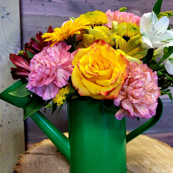 Cheerful mixed bouquet of yellow rose, pink carnations and white lilies in a green watering can