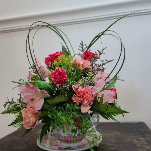 Pink floral arrangement in a teacup with heart-shaped loops