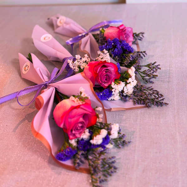 Three small pink rose bouquets wrapped in pastel paper with purple ribbon