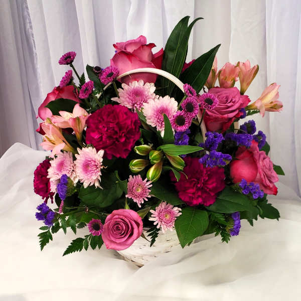 Basket arrangement of pink roses, carnations, and purple daisies