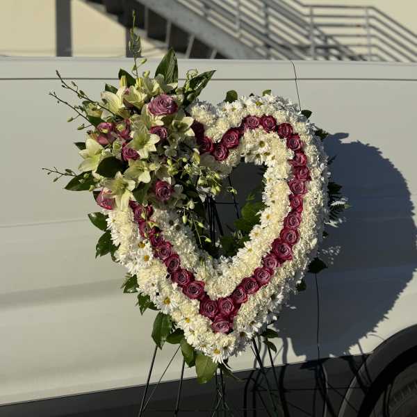 Heart-shaped floral wreath with pink roses and white flowers on an easel