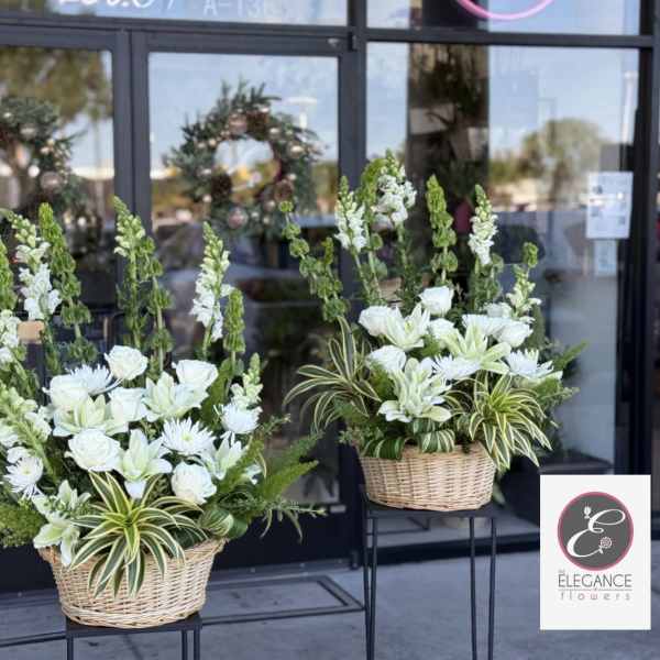 Two white floral arrangements in wicker baskets on stands
