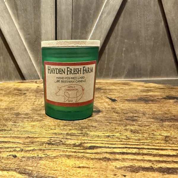 Green jar candle with an apple cinnamon label on a wooden surface
