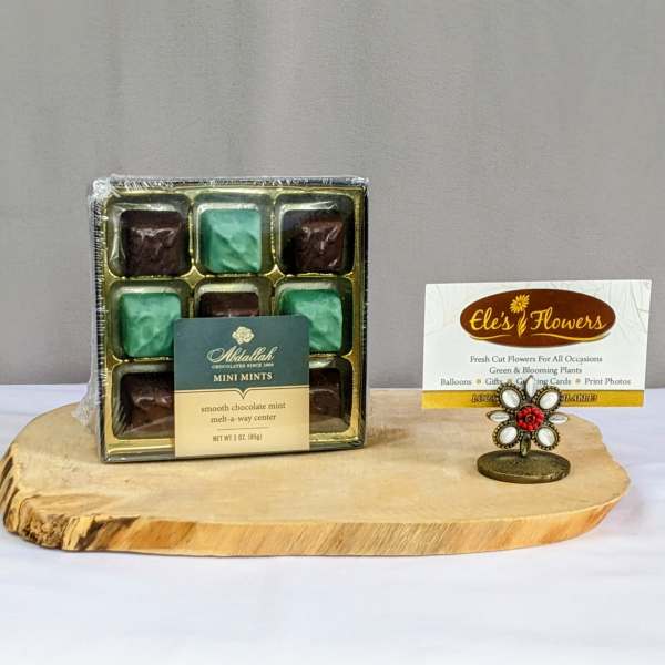 Box of chocolate mint candies on a wood tray beside a small card in a decorative holder