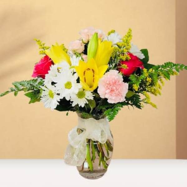 Mixed bouquet with yellow lilies, white daisies, pink roses, and carnations in a glass vase