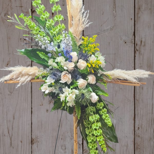 Floral cross arrangement with white roses, green orchids, and pampas grass