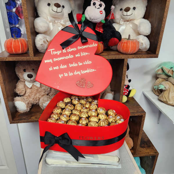 Heart-shaped red gift box filled with gold-wrapped chocolates and a Spanish message.